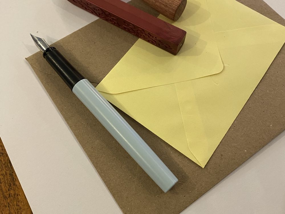 Una pluma estilográfica apoyada sobre un sobre amarillo y una hoja de papel.